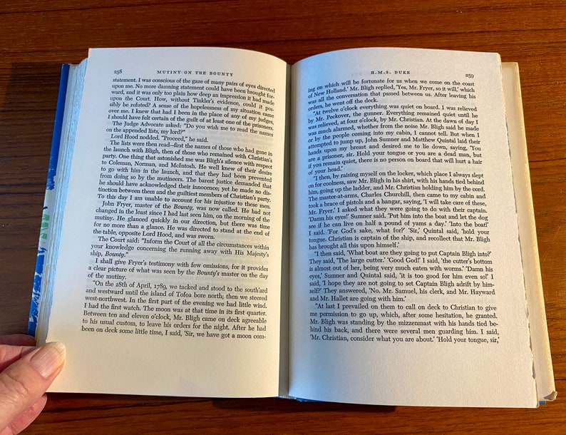K&ouml;nnte beinhalten: Eine Nahaufnahme eines ge&ouml;ffneten Buches mit einer vergilbten Seite, die Text aus dem Buch "Mutiny on the Bounty" von Kapit&auml;n Bligh zeigt. Der Text beschreibt die Ereignisse, die zur Meuterei auf der Bounty f&uuml;hrten.