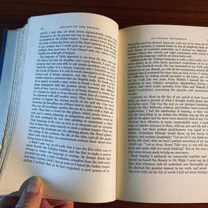 K&ouml;nnte beinhalten: Ein offenes Buch mit zwei sichtbaren Seiten. Die linke Seite tr&auml;gt den Titel "Mutiny on the Bounty" und die rechte Seite den Titel "An Indian Household". Beide Seiten haben Text in schwarzer Tinte.