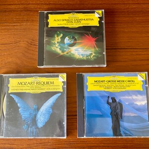 May include: Three compact discs with black cases and colorful artwork. The top CD features a red and orange sky with a blue planet. The middle CD has a blue angel with wings spread wide. The bottom CD has a white angel with wings spread wide against a blue sky.