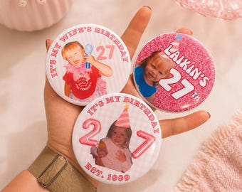 Könnte beinhalten: Drei runde Ansteckbuttons mit personalisierten Geburtstagsdesigns. Ein Button zeigt IT'S MY WIFE'S BIRTHDAY 27, ein anderer LAIKIN'S 27TH und der dritte IT'S MY BIRTHDAY 27 EST. 1999. Jeder Button enthält ein Kinderfoto und rosa Akzente.