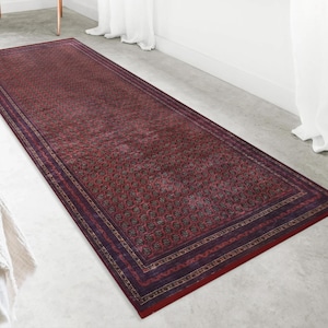 Peut inclure: Un long tapis rectangulaire de type chemin de couloir aux tons rouge foncé et bordeaux. Le tapis présente un motif géométrique dense et répétitif au centre, encadré par plusieurs bordures décoratives dans des nuances de rouge et de violet.