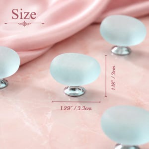 May include: Several oval-shaped, frosted light blue glass cabinet knobs with silver-toned metal bases. The knobs measure 1.29 inches in width and 1.18 inches in height, as indicated by the text and measurement lines visible in the image.