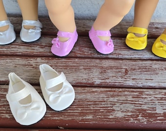Sapatos de boneca em couro sintético com laço, compatíveis com bonecas American Girl e Bitty Baby de 45 cm (18 polegadas), nas cores branco, amarelo, rosa e prateado.