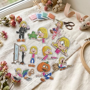 May include: A collection of embroidered patches featuring a cartoon character with blonde hair in various poses and outfits, including a skeleton costume, a pumpkin head, and casual clothing, alongside items like a frog, mirror, and cookies.