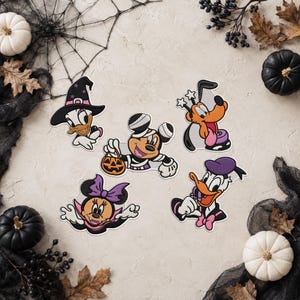Puede incluir: Cinco parches bordados con personajes de dibujos animados en disfraces de Halloween: un pato con sombrero de bruja, un ratón momia con un cubo de calabaza, un perro con varitas de estrella, un ratón vampiro y un pato con sombrero morado.