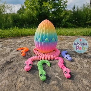 May include: A rainbow-coloured, scale-textured egg sits centrally, surrounded by five articulated, segmented toy snakes in orange, pink, green, and purple. A circular sticker with the text The Wonder Pals is positioned to the right of the egg.