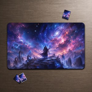 May include: A rectangular desk mat featuring a fantasy scene of a robed figure holding a staff on a rocky cliff under a vibrant purple and blue nebula sky with swirling galaxies, accompanied by three small matching rectangular cards.