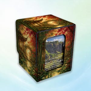 May include: A square deck box featuring a printed landscape of a traditional pavilion, bamboo, and red maple trees. A rectangular window on the front displays a trading card with a cliffside illustration and text including Mountain, Plains, and Swamp.
