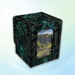May include: A square deck box featuring a dark, teal-toned illustration of a tentacled creature amidst ancient stone ruins. A rectangular cutout on the front displays a trading card showing a landscape with cliffs, green trees, and text.