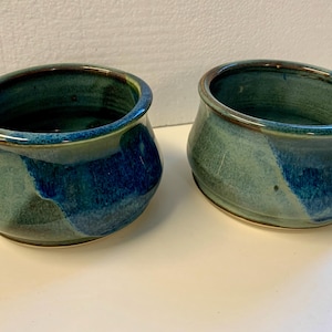 May include: Two small ceramic bowls with a blue and green glaze. The bowls are slightly flared at the top and have a rounded bottom.