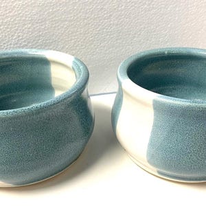 May include: Two ceramic bowls with a blue and white striped design. The bowls are round and have a slight lip around the rim.