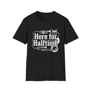 Könnte beinhalten: Ein schwarzes Kurzarm-T-Shirt mit einem weißen Grafikdruck von Musikinstrumenten, darunter eine Trompete, eine Trommel und eine Posaune. Der Text "Here for Halftime" ist mittig in einer fetten, weißen Schriftart aufgedruckt.