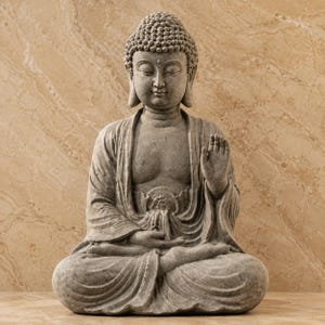 Puede incluir: Una estatua de color piedra gris de una figura de Buda sentada en pose meditativa. La figura presenta una superficie texturizada, una expresión facial serena con los ojos cerrados y la mano derecha levantada con la palma abierta.