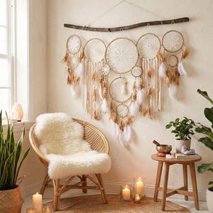 Peut inclure: Une grande décoration murale composée de plusieurs attrape-rêves circulaires interconnectés avec des toiles en dentelle blanche, suspendus à une branche en bois sombre. L'ensemble est orné de nombreuses plumes blanches et beiges.