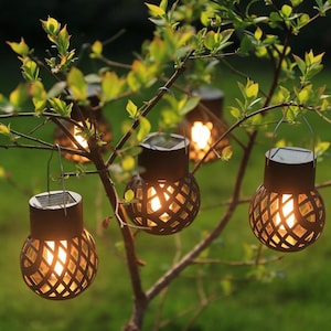 Peut inclure: Quatre lanternes solaires sphériques au design en cage grillagée marron foncé sont suspendues aux branches d'un arbre. Chaque lanterne possède un panneau solaire plat sur le dessus, une anse en métal et émet une lumière chaude et vive.