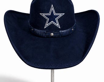 May include: A dark navy blue cowboy hat featuring a prominent white embroidered star on the front crown. The hat includes a matching dark navy blue band adorned with thin vertical leather-like strips and a small silver-toned circular metal stud.