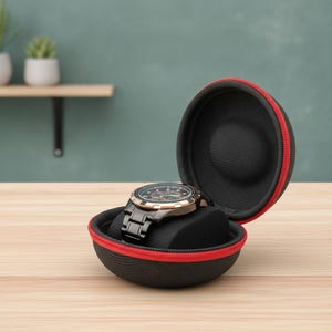 Puede incluir: Un estuche circular negro para reloj con cremallera roja, que presenta un exterior texturizado y un forro interior negro suave. Dentro del estuche abierto, un reloj de metal negro con esfera oscura descansa sobre un cojín de espuma.
