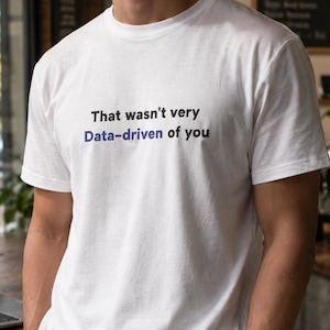 May include: A white short-sleeved t-shirt featuring the black and blue printed text That wasn't very Data-driven of you centered on the chest. The garment has a classic crew neckline and a standard fit, constructed from a plain white fabric.