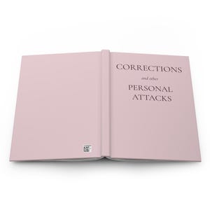 May include: An open book with a light pink cover. The right page features the dark text "CORRECTIONS and other PERSONAL ATTACKS" in a serif font. The left page contains a small square QR code near the bottom edge. The book is displayed flat.