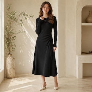 May include: A black long-sleeved midi dress featuring a ribbed knit texture, a round neckline, and a side drawstring detail that creates subtle ruching along the waist. The dress has a fitted bodice that transitions into a flared skirt silhouette.