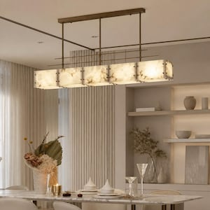 May include: A rectangular linear pendant light fixture featuring five square, translucent, cream-colored stone panels with natural veining. The light is suspended from the ceiling by a dark bronze metal frame with thin vertical and horizontal rods.