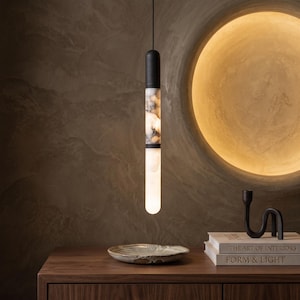 May include: A cylindrical pendant light fixture featuring a matte black top section, a central segment with a marbled white and grey pattern, and a translucent white bottom section that emits a soft glow, suspended by a thin black cord.