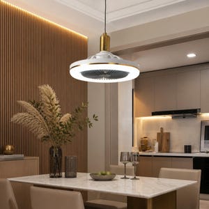 Puede incluir: Una lámpara colgante circular de techo con acabado en blanco y dorado y un ventilador integrado. El diseño incluye un soporte cilíndrico central de tono dorado y un anillo ancho iluminado que emite una luz blanca brillante.