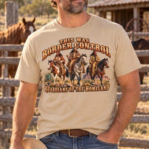 May include: A beige short-sleeved t-shirt featuring a graphic print of three individuals on horseback. The text reads "THIS WAS BORDER CONTROL" at the top and "GUARDIANS OF THE HOMELAND" at the bottom, with a desert landscape background.