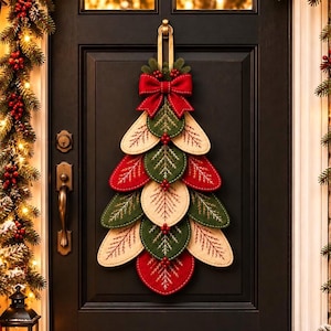 May include: A Christmas door hanging decoration shaped like a tree, constructed from layered, stitched fabric leaves in red, green, and cream colors. The ornament features a prominent red fabric bow at the top and is suspended by a gold-toned metal hook.