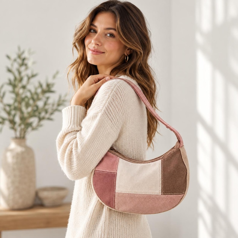 May include: A crescent-shaped shoulder bag featuring a patchwork design made of suede-like panels in shades of dusty rose, cream, and dark brown. The bag has a matching pink strap and a zipper closure along the top edge of the curved silhouette.