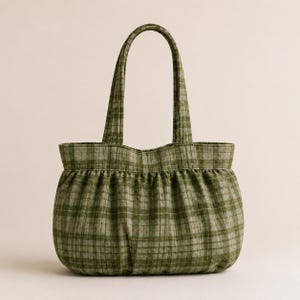 May include: A tote bag featuring a green and white plaid pattern. The bag has a rounded, gathered base with a soft, pleated texture and two matching fabric shoulder straps attached to the top edge of the main compartment.