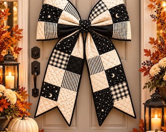 May include: A large quilted fabric bow decoration featuring a patchwork design of black and white patterns, including buffalo check, thin stripes, and celestial motifs with stars and crescent moons, displayed on a gray door.