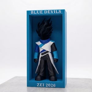 May include: A collectible figurine of a performer with a black spiky head, wearing a white and blue uniform with black trousers, displayed inside a blue rectangular box. The text BLUE DEVILS is at the top and ZEI 2026 is at the bottom of the box.