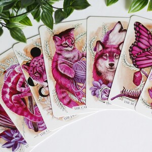 Pink and purple tarot and oracle cards featuring animals, flowers, plants and crystals.