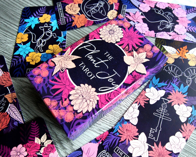 Tarot and oracle cards featuring illustrations on a dark background with brightly colored flowers.