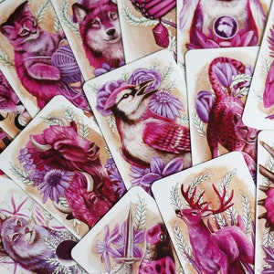 Pink and purple tarot and oracle cards featuring animals, flowers, plants and crystals.