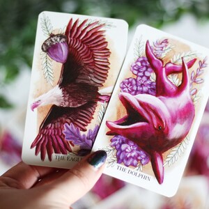 Pink and purple tarot and oracle cards featuring animals, flowers, plants and crystals.