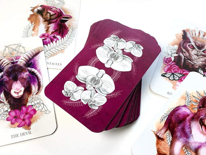 A stack of tarot cards with a pink back with orchid drawings.