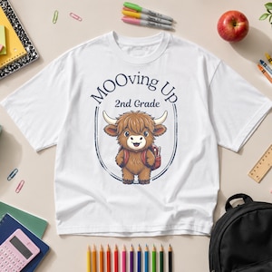 May include: A white short-sleeve t-shirt featuring a graphic of a brown Highland cow wearing a backpack. The text above the cow reads MOOving Up 2nd Grade in dark blue lettering, all enclosed within a dark blue oval border design.