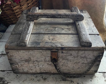 May include: A weathered wooden box with a hinged lid, metal clasp, and chain. The box has a handle on top and is painted in a distressed white finish. The box is likely vintage or antique, and is suitable for storage.
