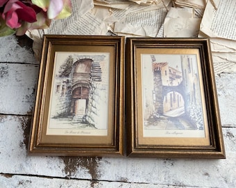 May include: Two framed vintage prints of European streetscapes. The left print shows a stone archway with the text "Les Ruelles de Provence". The right print shows a narrow street with the text "Rue villageoise".