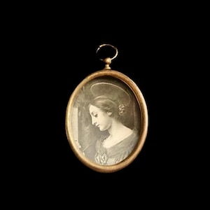 May include: A gold-toned oval locket with a black and white image of a woman inside. The woman is wearing a white dress and has her hair pulled back.