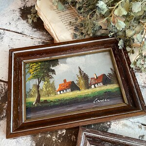 May include: A framed painting of a countryside scene with two houses, a tree, and a blue sky. The painting is signed "Carice" in the bottom right corner.