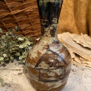 May include: A brown ceramic vase with a white and black geometric design. The vase has a narrow neck and a wide base.