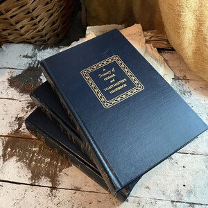 Puede incluir: Una pila de tres libros de tapa dura de color azul marino con letras doradas. El libro de arriba tiene el t&iacute;tulo "A Treasury of Humor and Toastmasters Handbook".