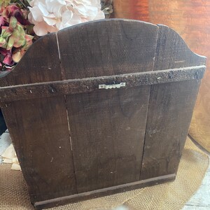 Pu&ograve; includere: Un ripiano a muro in legno marrone scuro con la parte superiore curva e un gancio di metallo sul retro. Il ripiano &egrave; appoggiato su una superficie di juta.