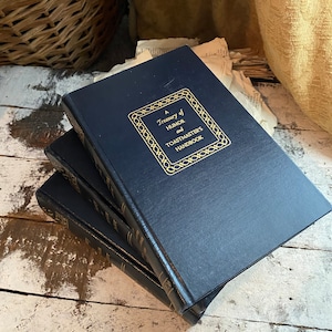 Puede incluir: Tres libros de tapa dura de color azul marino apilados sobre una superficie de madera blanca. El libro de arriba tiene letras doradas que dicen "A Treasury of Humor and Toastmasters Handbook".