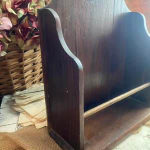 Pu&ograve; includere: Un porta riviste in legno marrone scuro con uno scaffale e un'asta di metallo. Il porta riviste ha una parte superiore curva ed &egrave; fatto di legno con venature naturali.