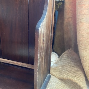 Pu&ograve; includere: Un porta riviste in legno marrone scuro con uno scaffale e una parte superiore decorativa. Il porta riviste &egrave; in legno con una finitura naturale e ha un aspetto rustico.