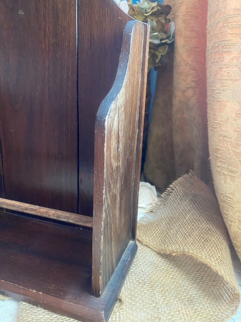 Pu&ograve; includere: Un porta riviste in legno marrone scuro con uno scaffale e una parte superiore decorativa. Il porta riviste &egrave; in legno con una finitura naturale e ha un aspetto rustico.